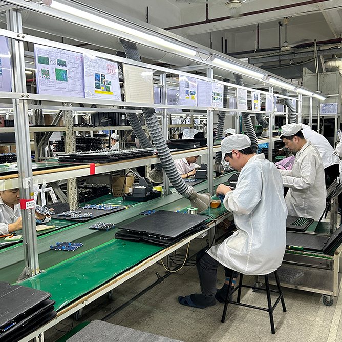 Workers assembling boards at a through-hole line with fume extractors over the benches